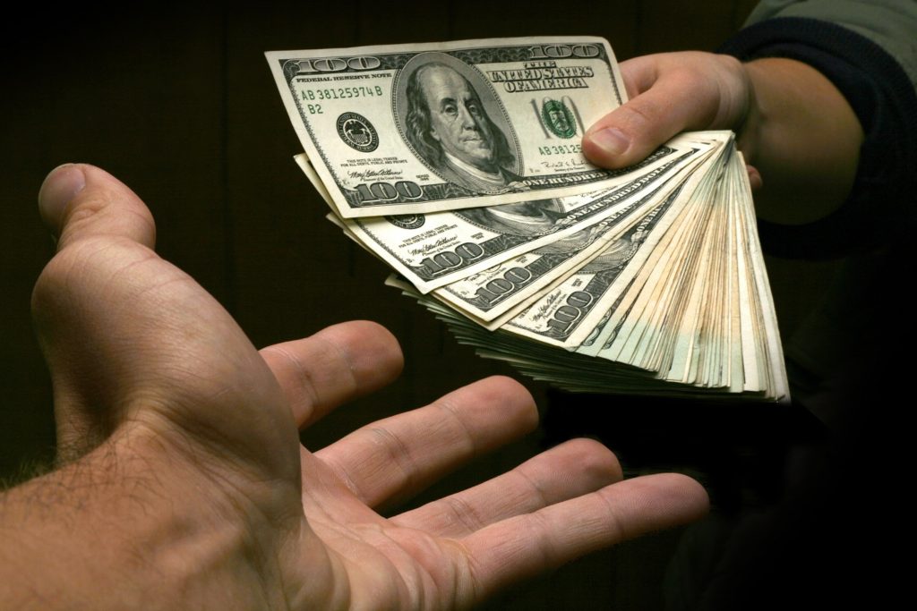 A stack of cash being handed over from one hand to another.